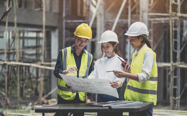 Разнообразная команда экспертов планирует на строительной площадке. Проект недвижимости с инженерами-строителями, архитекторами, бизнес-инвесторами и генеральным штатом обсуждают детали планов