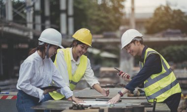 Asian woman civil engineer paper plan building architect wearing white safety helmet look at contruction site.Female foreman in a construction helmet, facemask