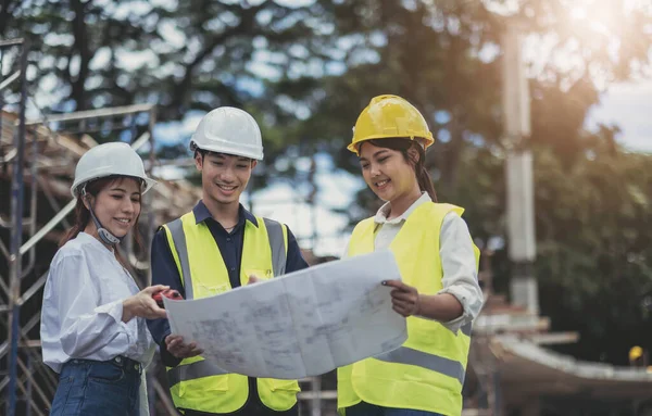 Three experts inspect commercial building construction sites and construction site holding blueprint