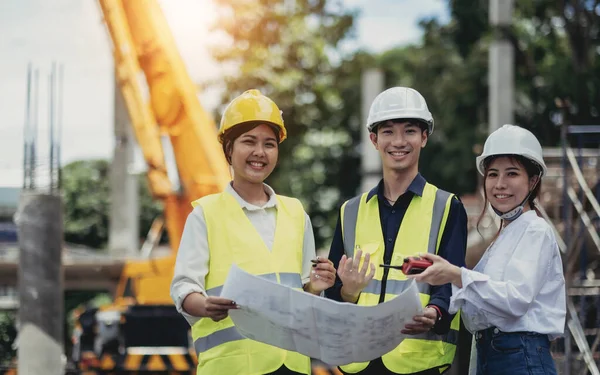 Three experts inspect commercial building construction sites and construction site holding blueprint