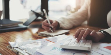 Cropped shot of woman hand using calculator while sitting at office desk, vertical view