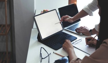 Two businesswomen meet in a meeting room for a business consultation, using a laptop computer and tablet. mockup of a laptop with a blank scree