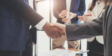 Two  business men shaking hands while their colleagues applauding in the backgroun