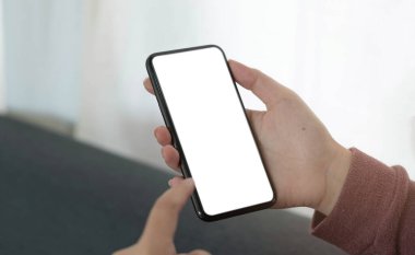 Mockup image blank white screen cell phone.women hand holding texting using mobile on sofa