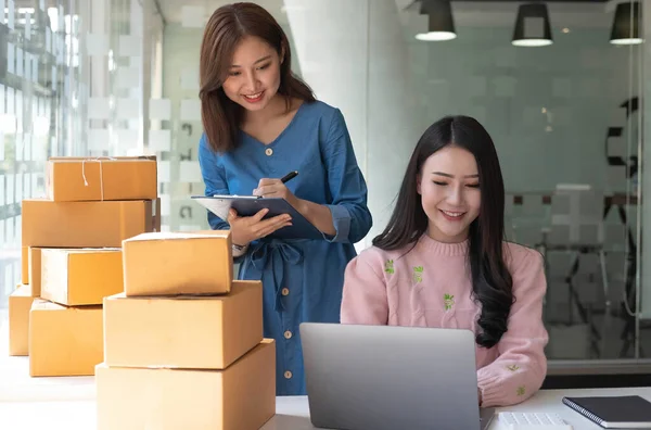 Portrait of Starting small businesses SME owners, two Asian woman check online orders Selling products working with boxs freelance work at home office, sme business online small medium enterpris