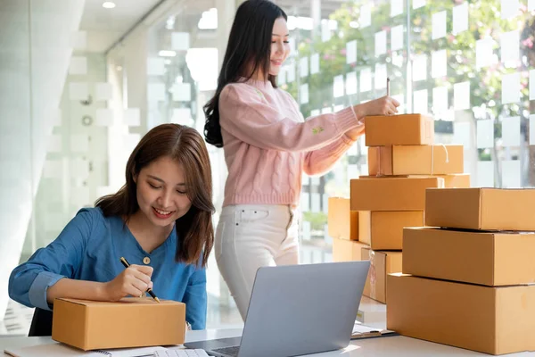 Portrait of Starting small businesses SME owners, two Asian woman check online orders Selling products working with boxs freelance work at home office, sme business online small medium enterpris