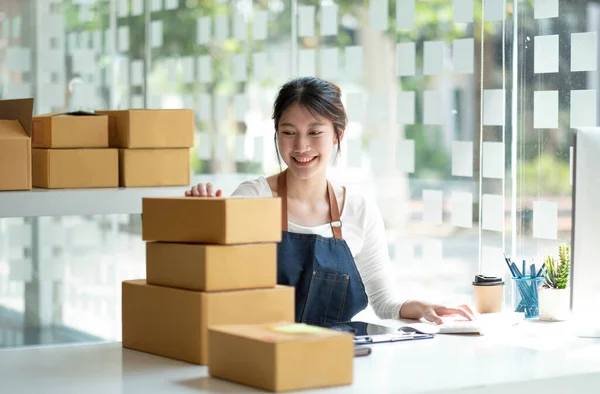 Startup SME small business entrepreneur SME or freelance Asian woman using a laptop with box, Young success Asian woman with her hand lift up, online marketing packaging box and delivery, SME concept