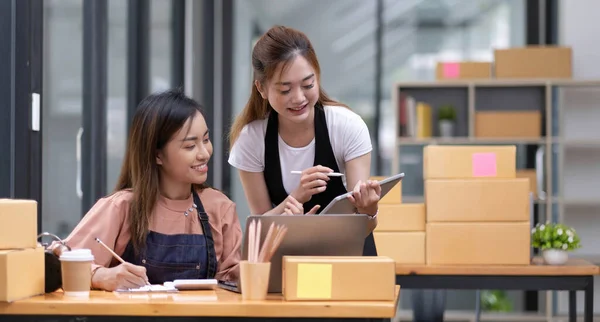 Portrait of Starting small businesses SME owners, two Asian woman check online orders Selling products working with boxs freelance work at home office, sme business online small medium enterpris