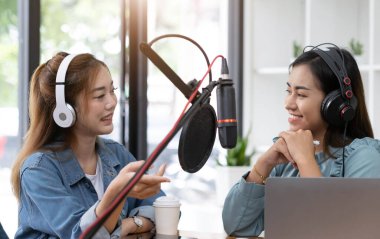 Smile two asian young woman, man radio hosts in headphones, microphone while talk, conversation, recording podcast in broadcasting at studio together. Technology of making record audio concept