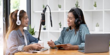 Smile two asian young woman, man radio hosts in headphones, microphone while talk, conversation, recording podcast in broadcasting at studio together. Technology of making record audio concept