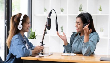Smile two asian young woman, man radio hosts in headphones, microphone while talk, conversation, recording podcast in broadcasting at studio together. Technology of making record audio concept
