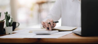 Hesap makinesi kullanan, aylık ev bütçesini yöneten, vergi veya faturaları özetleyen, gelecekteki yatırımları planlayan, evde mali işler yapan, muhasebe kavramını işleten genç bir kadın.