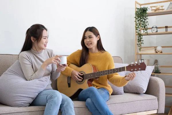 A young woman playing guitar on the sofa in the living room. Young Asian loving lovers couple bonding at home, relaxing on sofa the living room