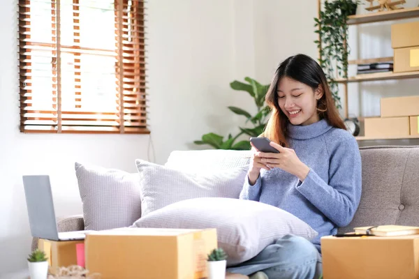 Asian business woman on sofa using a laptop computer checking customer order online shipping boxes at home. Starting SME Small business entrepreneur freelance. Online business, SME Work home concept