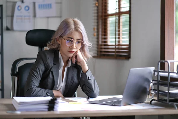 Tired business asian woman holds her fingers on her temples at work table. Irregular working day stressed worried, tired and overwhelmed concep