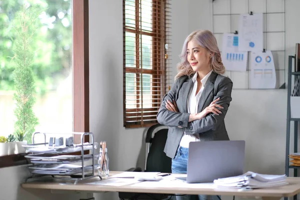 Young confident smiling Asian business woman leader, successful entrepreneur, elegant professional company executive ceo manager. Asian business woman is standing in office with arms crossed
