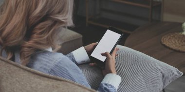 Yakın plan görüntü, güzel Asyalı bir bayan oturma odasında dinlenirken akıllı telefonunu kullanıyor. Elinde cep telefonu beyaz ekran modeli olan bir kadın.