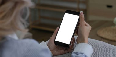 Yakın plan görüntü, güzel Asyalı bir bayan oturma odasında dinlenirken akıllı telefonunu kullanıyor. Elinde cep telefonu beyaz ekran modeli olan bir kadın.