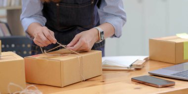 Küçük bir girişim konsepti. Paket kutusundaki ipleri bağlayan kadın siparişe hazırlanmak için eşyaları paketliyor. E-ticaret satıcıları için nakliyeye hazırlanılıyor