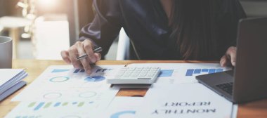 Hesap makinesi kullanan, grafik çizelgesiyle çalışan ve iş stratejisini, mali istatistiği, masa başında dikey görünümü analiz eden bir kadın eli görüntüsü.