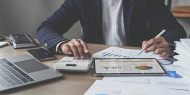 İş adamı modern ofiste masa başında iş planı yazıyor. Planlama, yatırım, iş stratejisi ve pazarlamayı grafik şeması ve dijital tablet kullanılarak analiz eder