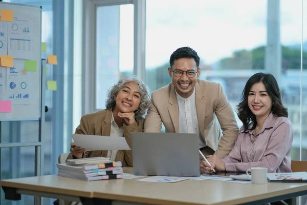Group of Asia young creative people in smart casual wear smiling in creative office workplace. Diverse Asian male and female stand together at startup. Coworker teamwork concept..