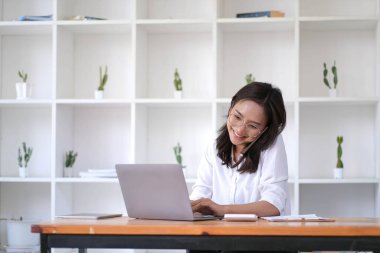 Akıllı telefondan konuşan Asyalı genç iş kadınının portresi ofis bilgisayarına dizüstü bilgisayar yaz. Masa başındaki güzel kız eve sipariş veriyor. Girişimci Asyalı kadın çevrimiçi sme tele pazarlama..