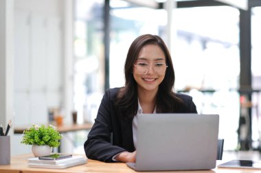 Genç Asyalı iş kadını modern ofiste tablet kullanarak çalışmaktan memnun...