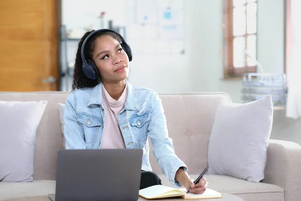 Smiling Asian young female using headphones looking at laptop screen listen and learning online courses