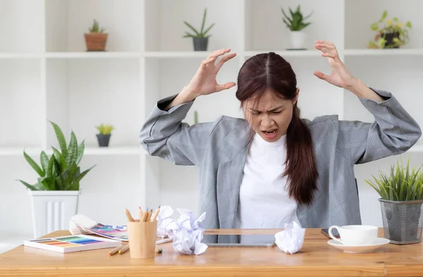 Mad Angry Stressed young asian female graphic designer or businesswoman with a crumpling paper on the table dissatisfied with her work, complained from her boss, getting a job problem..