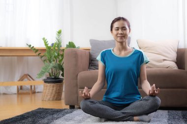 Gülümseyen Asyalı kadın oturma odasında yoga yapıyor, internetten omuzlarını esnetiyor. COVID-19 sırasında evde kişisel izolasyon ve egzersiz..