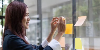 Close-up of a woman hand holding a pen affixing a note to her mirror at the office..