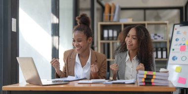 Two young Asian business woman talk, consult, discuss working with new startup project idea presentation analyze plan marketing and investment in the office..