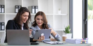 Two young Asian business woman talk, consult, discuss working with new startup project idea presentation analyze plan marketing and investment in the office..
