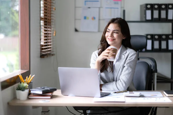 Young woman working on a laptop in the office. Asian businesswoman sitting at her workplace in the office. Beautiful Freelancer Woman working online at her home