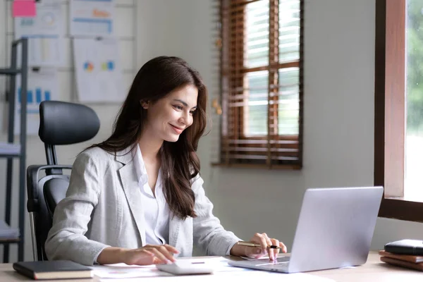 Young woman working on a laptop in the office. Asian businesswoman sitting at her workplace in the office. Beautiful Freelancer Woman working online at her home