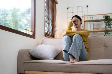 Kanepede oturan mutsuz Asyalı genç kızın tapınaklarında el ele tutuşmak. Hastalığı ve baş ağrısı yüzünden kendini pek iyi hissetmiyor. Cepheden görüldü. Stres ve hastalık konsepti...