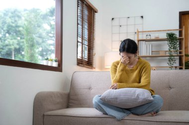 Kanepede oturan mutsuz Asyalı genç kızın tapınaklarında el ele tutuşmak. Hastalığı ve baş ağrısı yüzünden kendini pek iyi hissetmiyor. Cepheden görüldü. Stres ve hastalık konsepti..