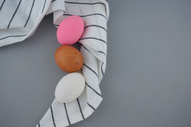 Güzel renkli yumurtalar, beyaz, kahverengi ve pembe natürmort yaşam, desenli çay havlusu bezi düz gri arka planda yatıyordu..