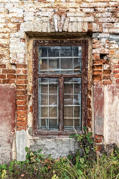 窗玻璃上有一座废弃的老房子的窗格 窗框上有剥落的油漆 砖块随着时间的流逝而磨损 — 图库照片