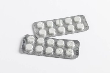 Tıbbi reçeteye göre tabletler, beyaz bir zemin üzerinde folyo ve plastik dolu bir paketin içinde.