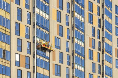 Üniformalı işçiler, inşaatta beşikte, yüksek bir binanın ön cephesinde işlerini yaparlar.