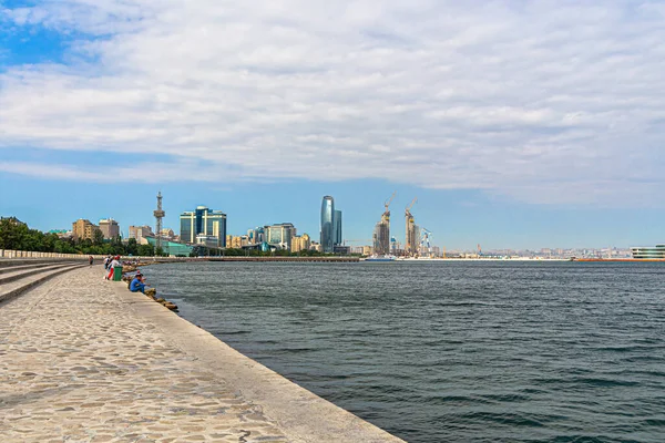 Bakü, Azerbaycan, 07.26.2019. Primorsky Bulvarı 'nın setinde insanlar körfezin kıyısında dinleniyor. Bakü Körfezi 'nde arka planda şehir evleri silueti var.