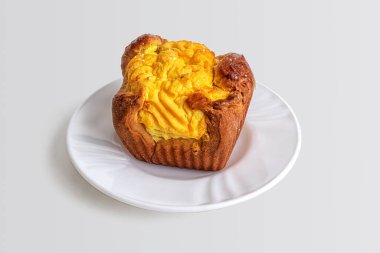 Kek, süzme peynirli, altın rengine boyanmış, küçük beyaz bir tabakta. Tatlı tatlı