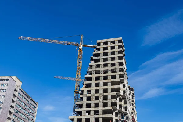 青い空を背景に 建設中の複数階建ての建物のコンクリートブロック上の建設クレーンの矢印 — ストック写真