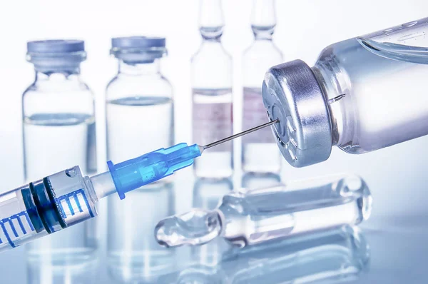 Şırınga ve farklı türde ampul ve şişeler beyaz arkaplandaki yansıma ile yakın plan