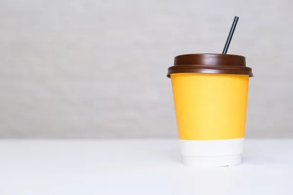 Kahverengi kapaklı sarı kağıt kullan-at kahve fincanı ve beyaz zemin üzerinde pipet fotokopi alanı olan beyaz tuğla duvara karşı..