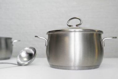 Paslanmaz çelik kap, saksı ve beyaz masada bir kepçe, zararsız çevre dostu mutfak aletleri, insanlar için zararsız..