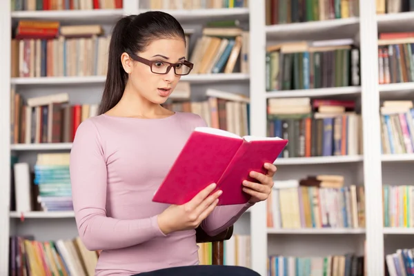 Förvånad ung kvinna läser en bok — Stockfoto