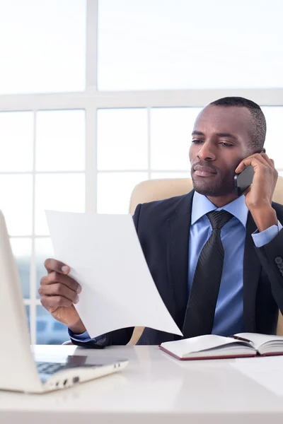 Afrikanischer Geschäftsmann telefoniert mit dem Handy und überprüft Dokumente — Stockfoto